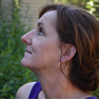 Frau mit braunen Haaren zeigt nach oben, betrachtet nachdenklich die Umgebung.